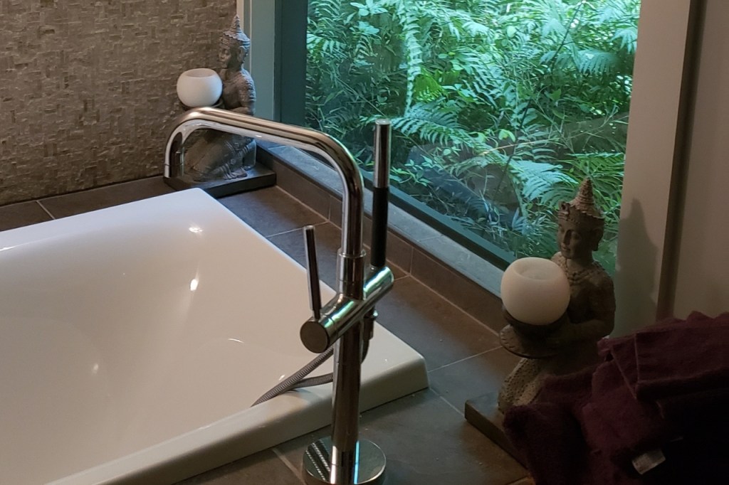 Freestanding soaking tub with sleek chrome faucet beside large window with natural forest view