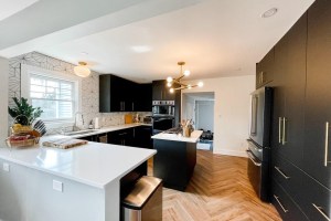 Modern black and white kitchen with island, chevron wood floors, and gold light fixture