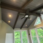 Vaulted ceiling sunroom with large windows, wood beams, and modern ceiling fan