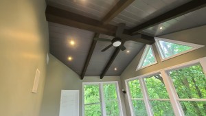Vaulted ceiling sunroom with large windows, wood beams, and modern ceiling fan