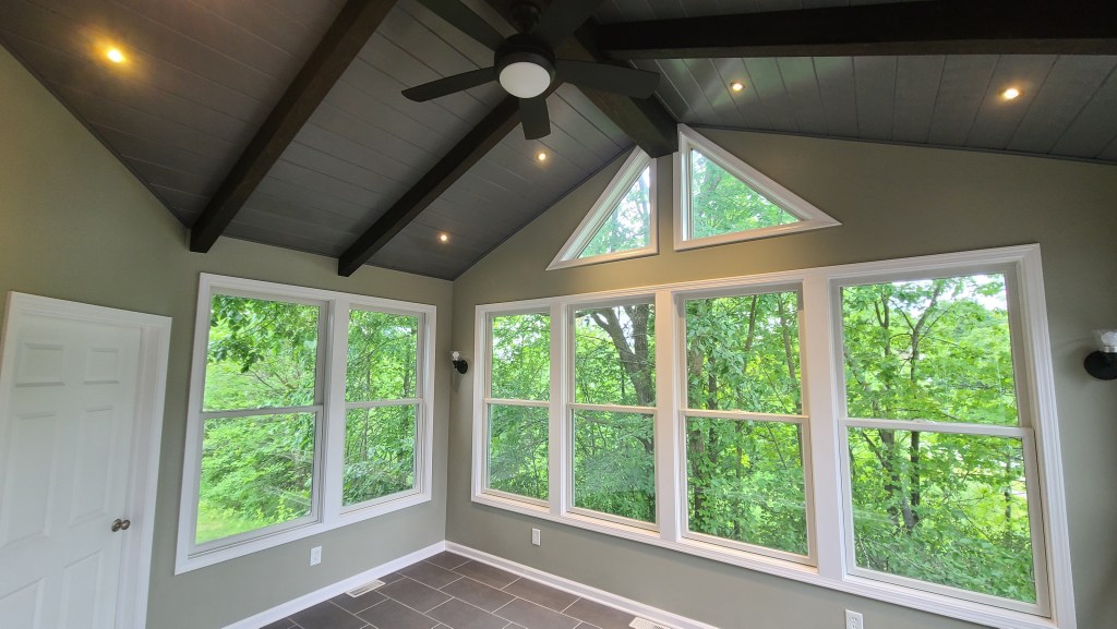 Four-season sunroom with vaulted ceiling, fan, and large windows overlooking trees