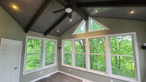 Four-season sunroom with vaulted ceiling, fan, and large windows overlooking trees