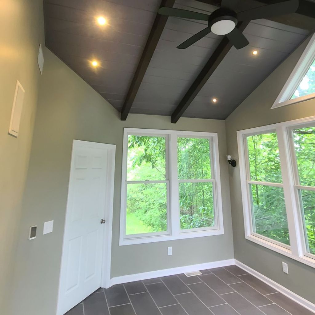 A bright sunroom with large windows, tile flooring, and a vaulted ceiling with dark wood beams and recessed lighting, completed by Butler Building, a general contractor in Akron.