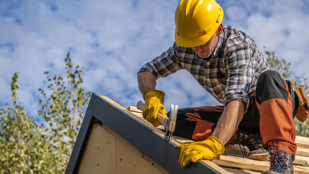 A remodeling contractor wearing a yellow hard hat and gloves, working on a roof under a clear sky in Akron.