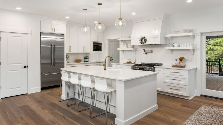 Modern white kitchen with an island, pendant lighting, stainless steel appliances, and hardwood flooring.