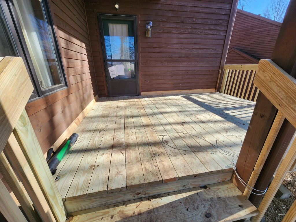Freshly repaired wood deck with railing outside a brown exterior home