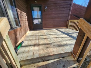 Freshly repaired wood deck with railing outside a brown exterior home