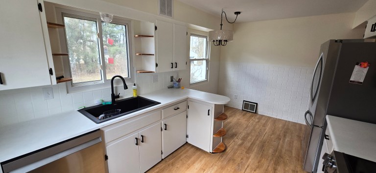 Corner kitchen remodel with black sink, white cabinets, and wood floors by kitchen remodel contractors