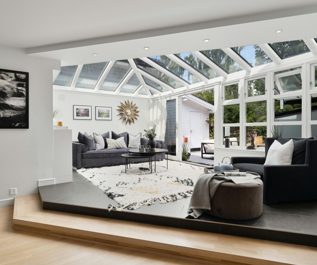 Cozy sunroom interior with glass roof, modern gray sofa, decorative wall art, and natural light – home addition remodel in Northeast Ohio by Butler Building.