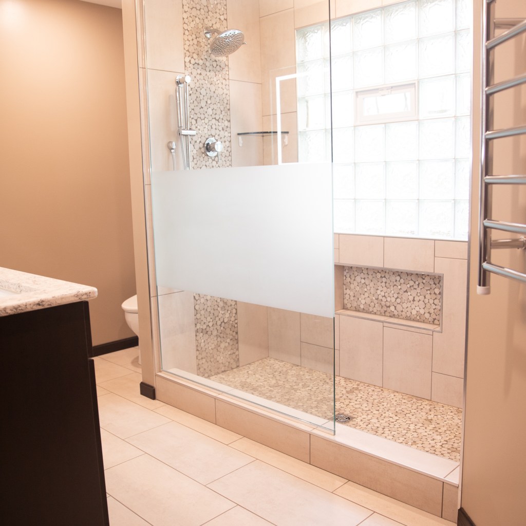Walk-in shower with glass panel, tiled walls, pebble shower floor, and built-in niche completed by local remodeling contractors.