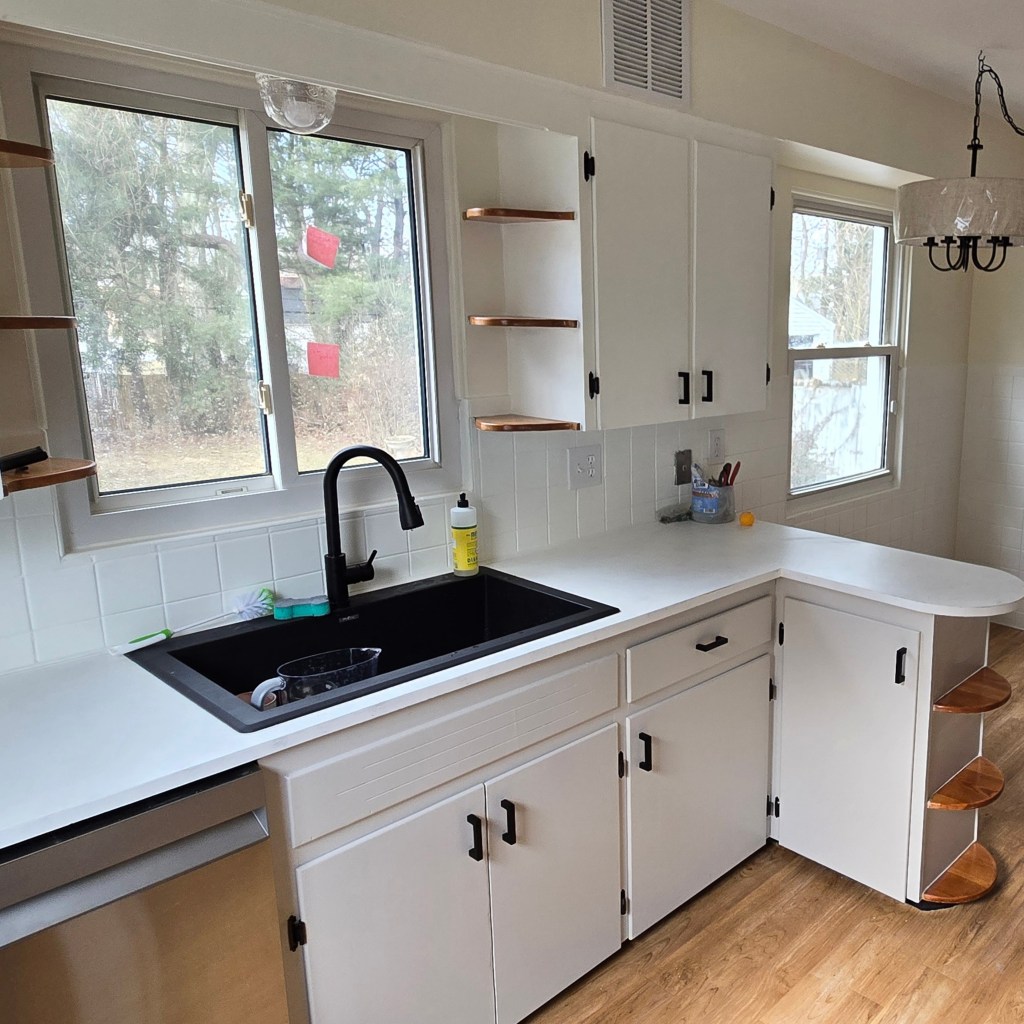 Modernized kitchen with white cabinets, black hardware, wood-look flooring, black faucet, and stainless-steel appliances.
