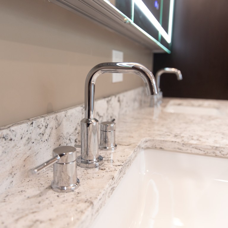 Close-up of chrome bathroom faucet and quartz countertop with undermount sink in modern bathroom remodel.