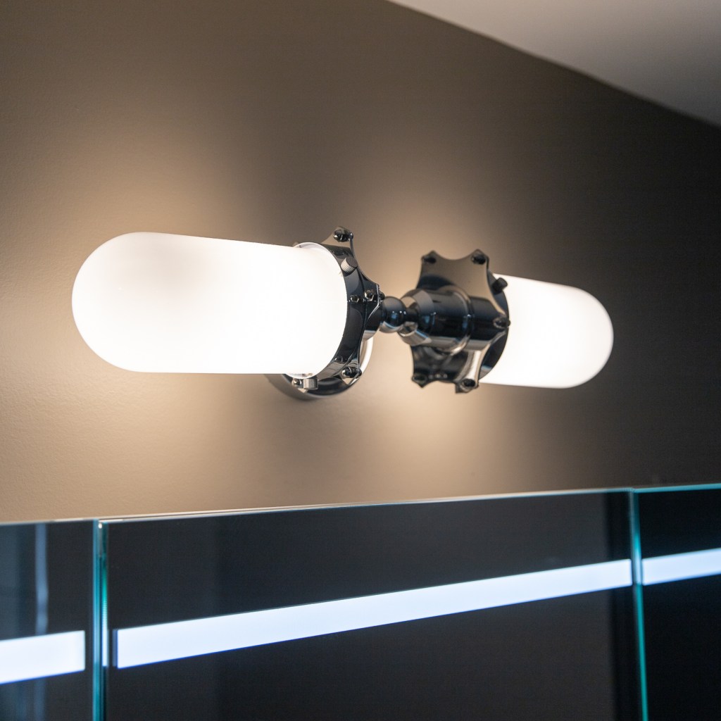 Modern bathroom vanity light fixture with frosted glass shades installed above LED mirror.