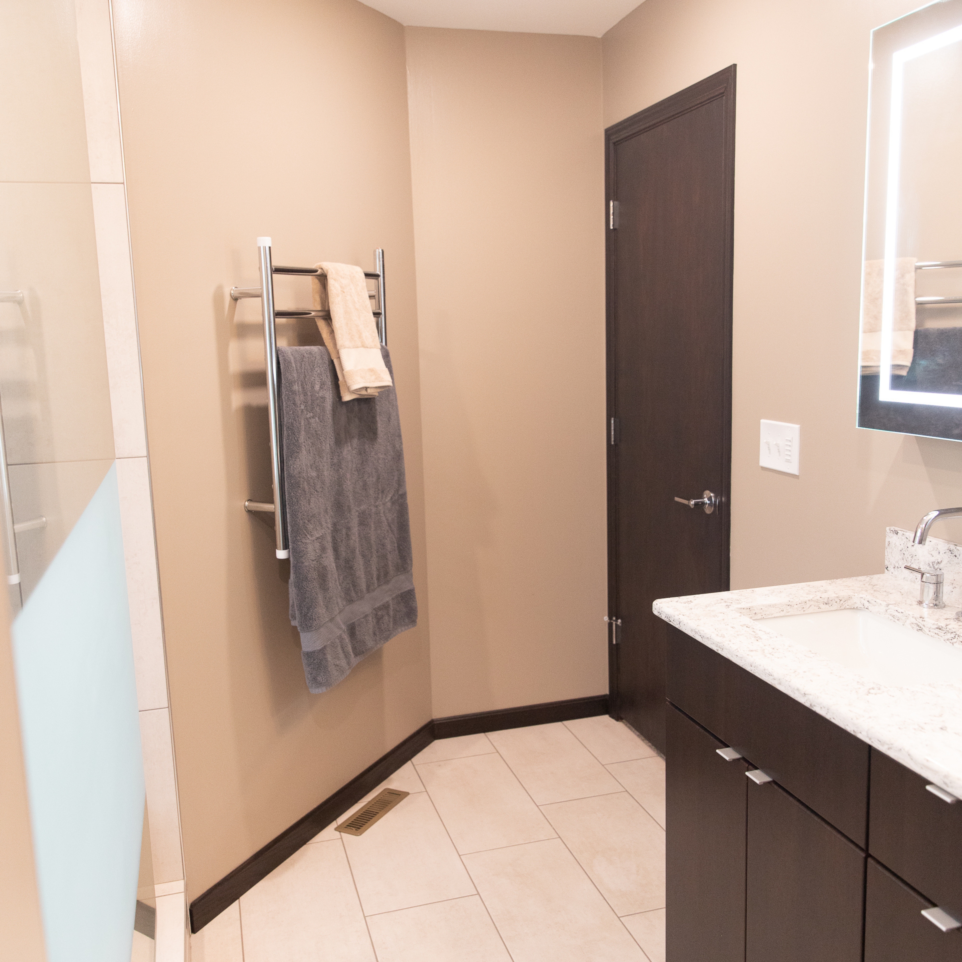 Chrome heated towel rack mounted on bathroom wall in a modern bathroom remodel.