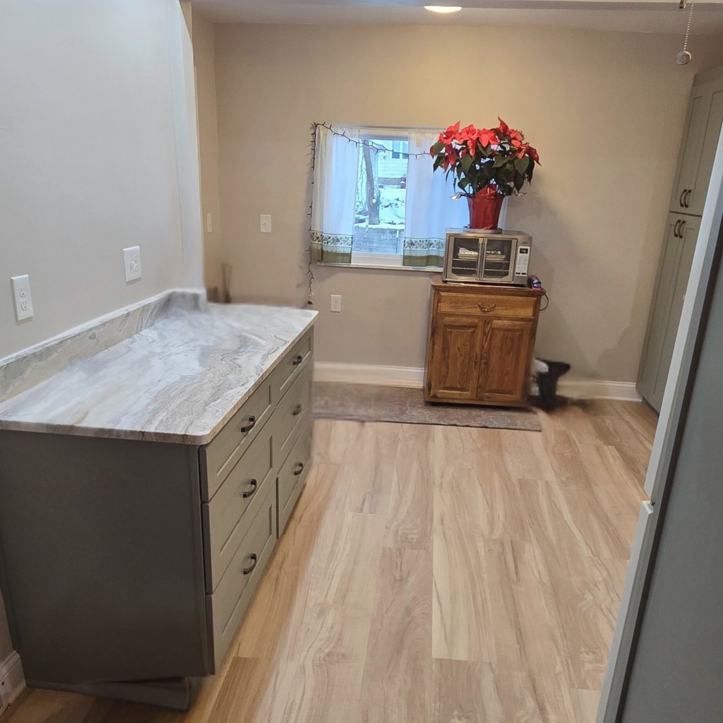 Kitchen featuring new sage green lower cabinets with a marble-look countertop, LVP flooring, and a window letting in natural light.