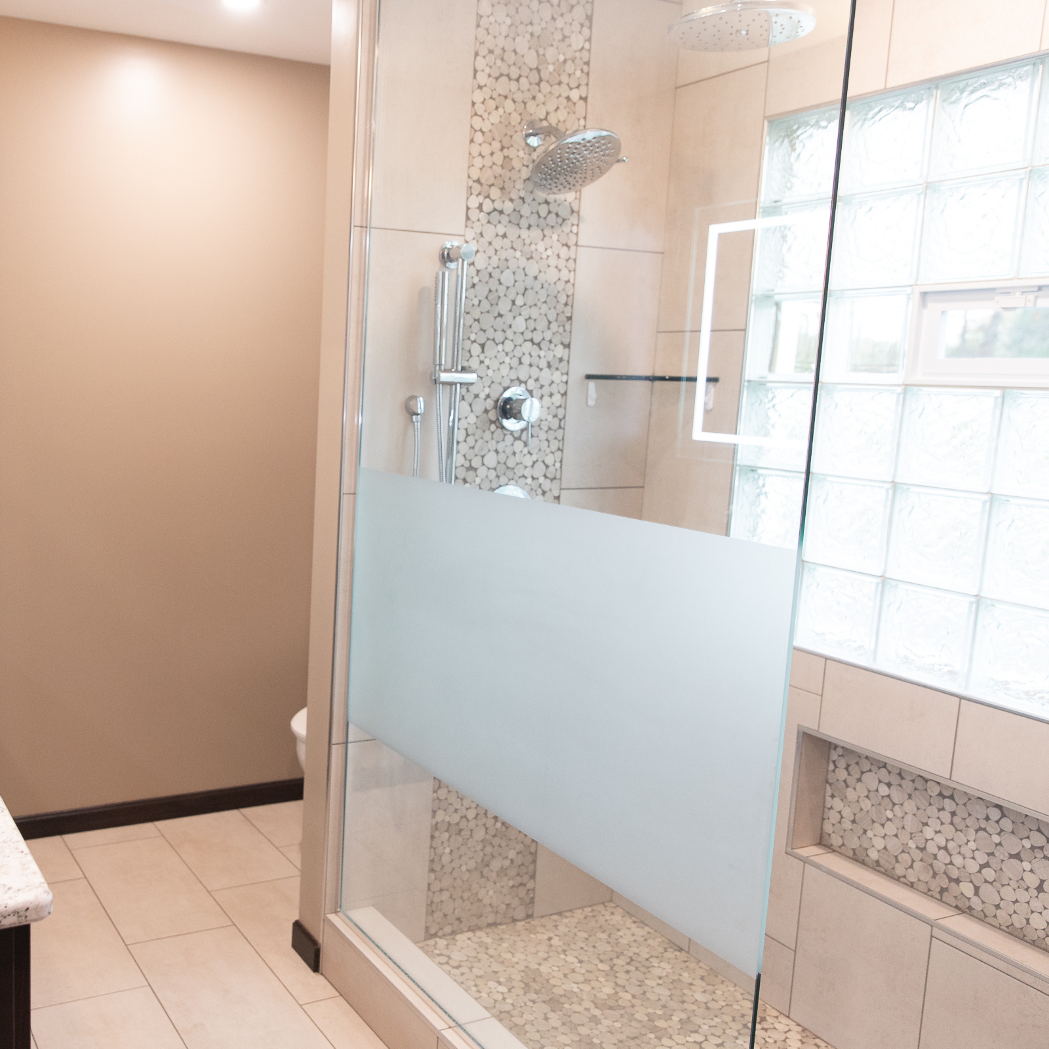 Frameless glass shower enclosure with frosted privacy panel and pebble tile shower floor.