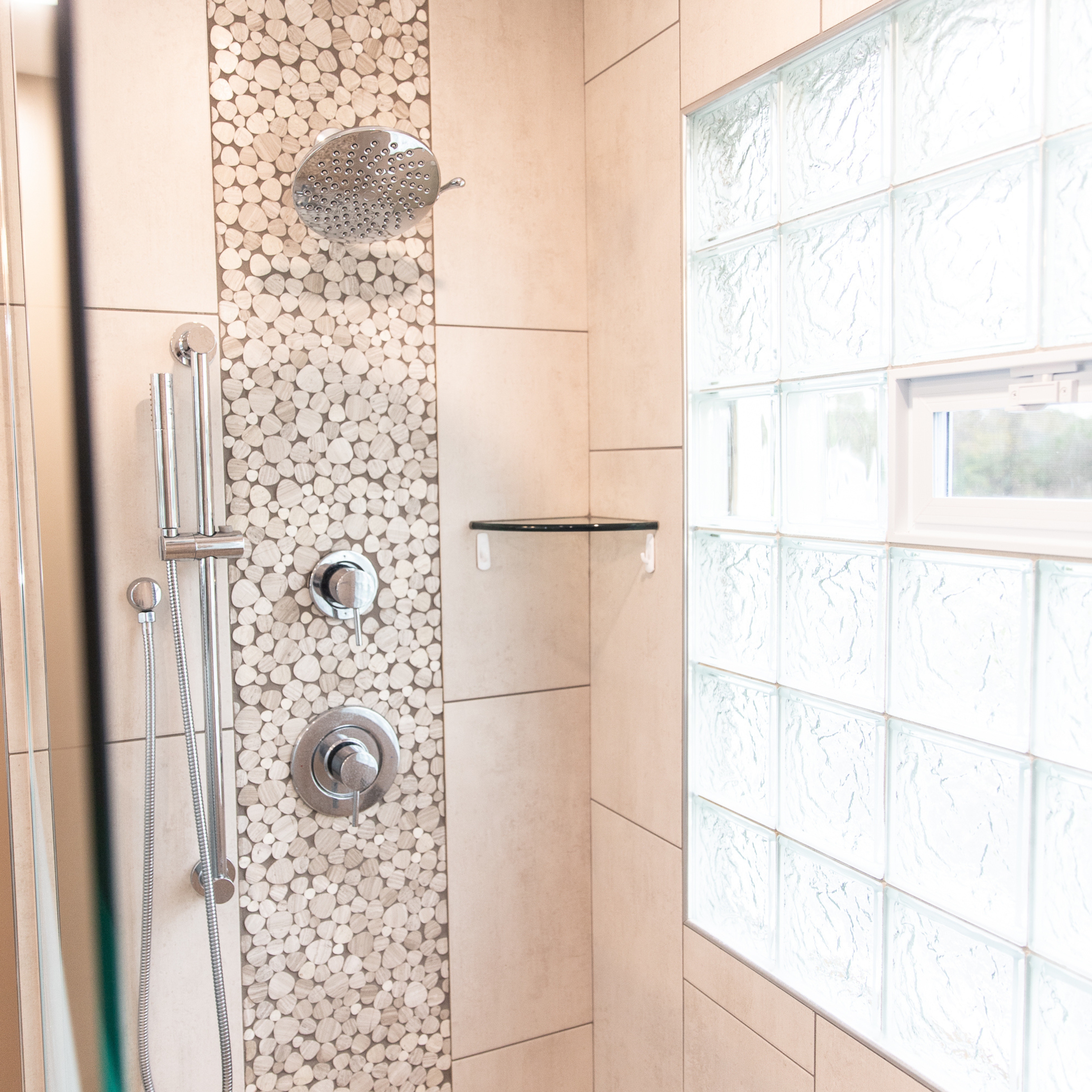 Rainfall showerhead, handheld shower, and pebble tile accent wall in a custom walk-in shower.