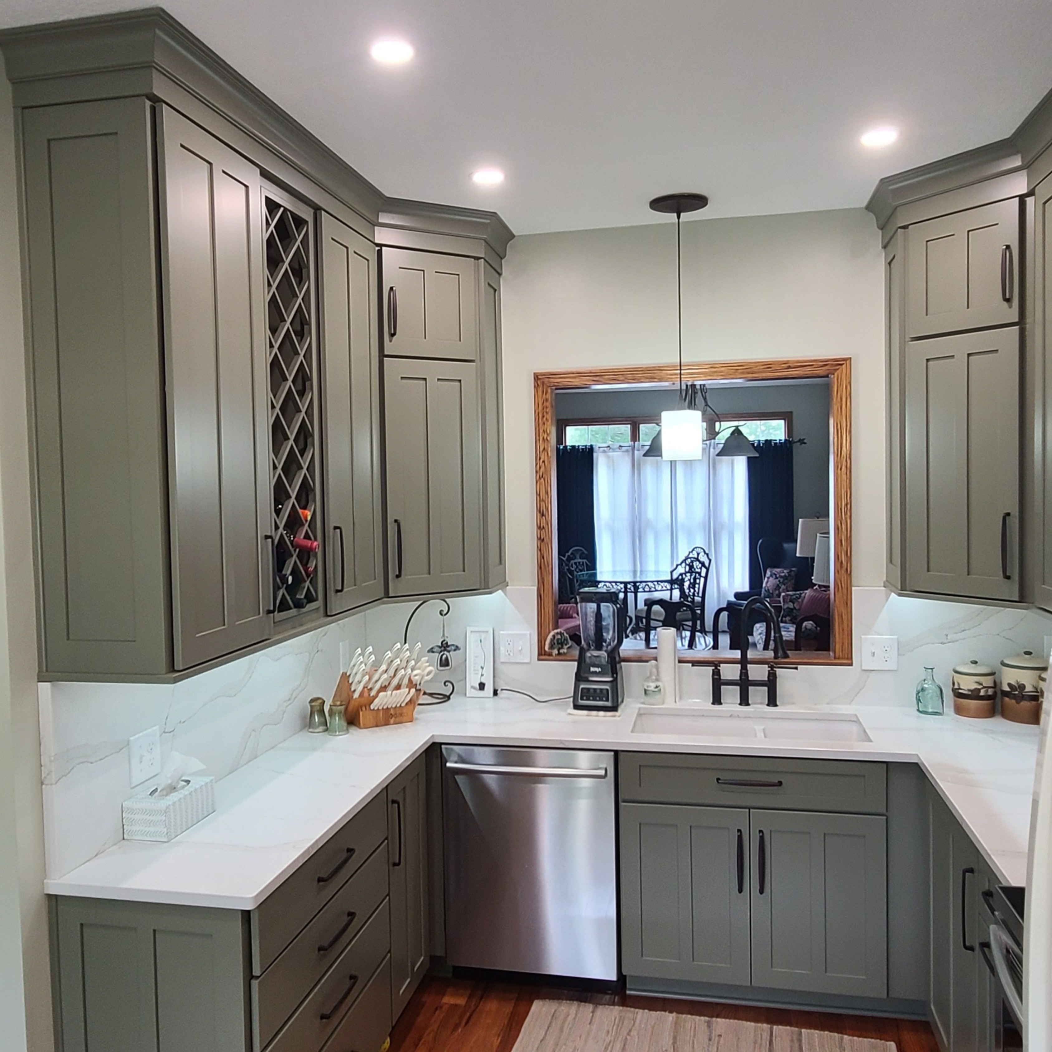 Bright remodeled kitchen with sage green Shaker cabinets, white quartz countertops, stainless steel appliances, recessed lighting, and a pendant light over the sink.