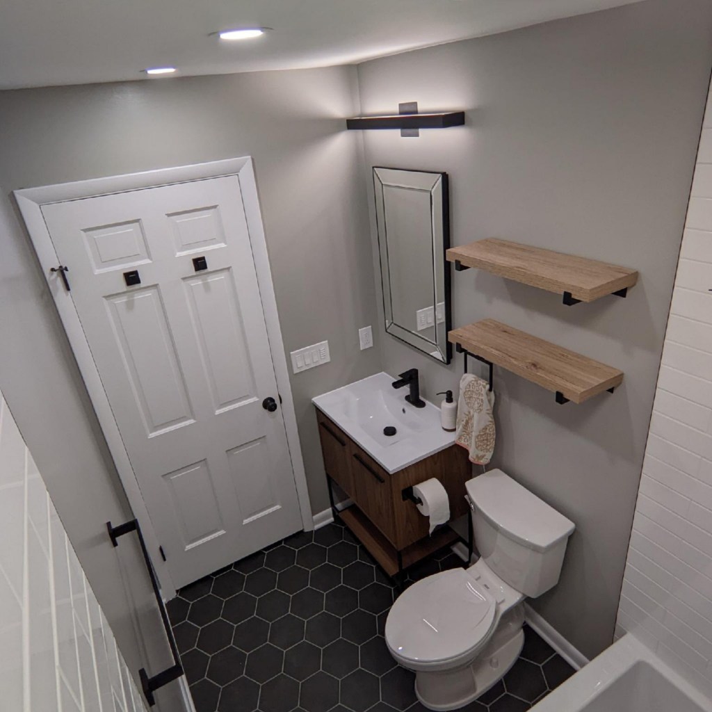 Fully remodeled bathroom featuring tiled shower, modern vanity, black fixtures, updated lighting, and new flooring by a local remodeling contractor.