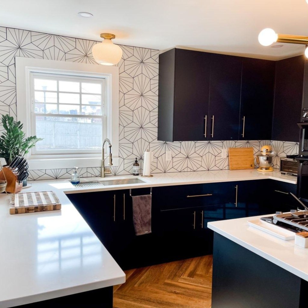 Contemporary kitchen with matte-black lower cabinets, white quartz countertops, a geometric tile backsplash, under-cabinet lighting, and brass hardware around the sink area.
