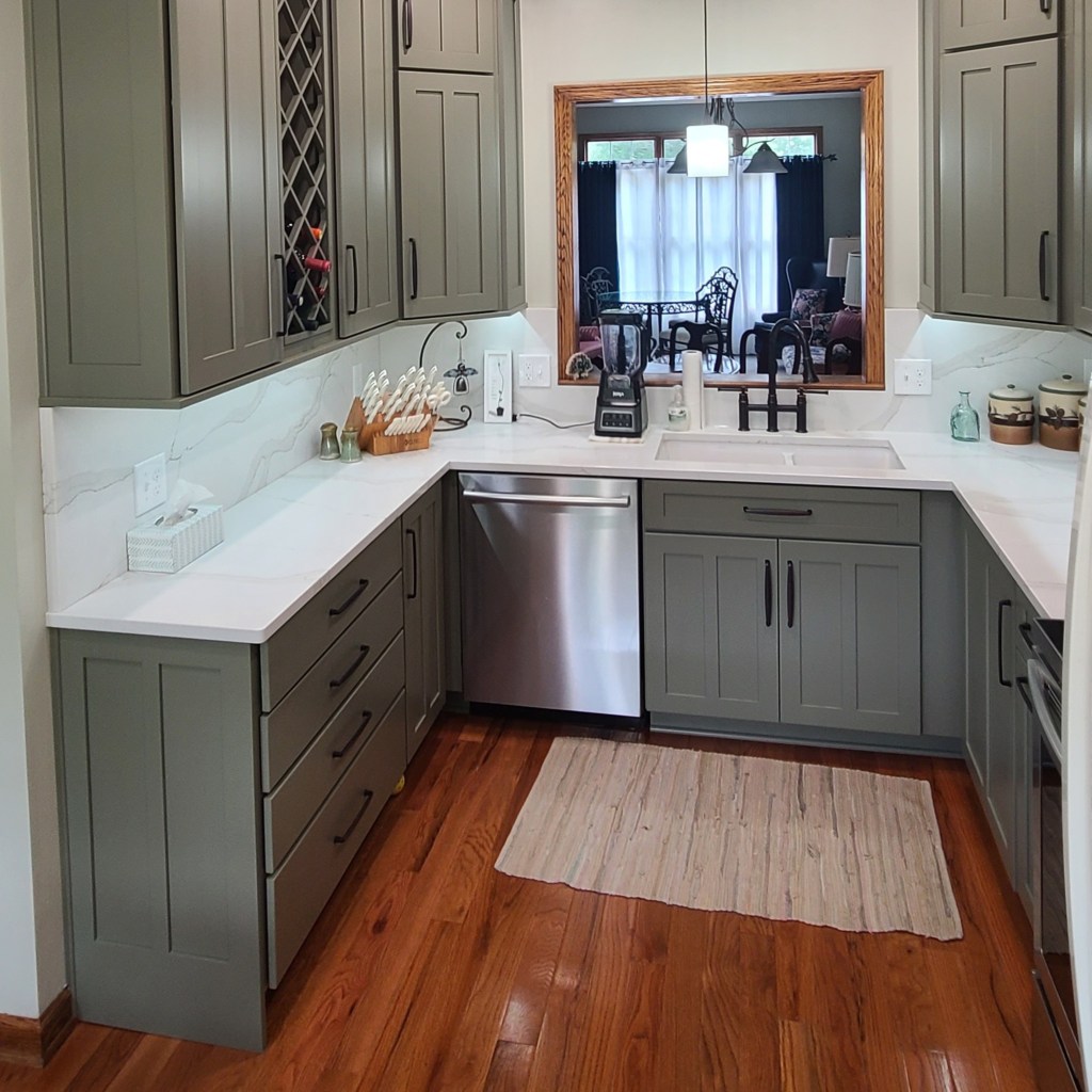Modern kitchen featuring sage green cabinets, built-in wine rack, quartz countertops, stainless dishwasher, and a black faucet.