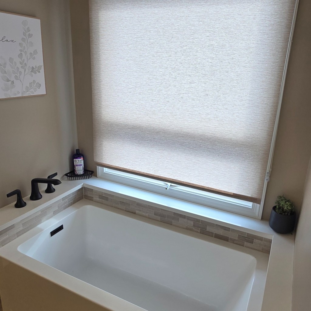 Freestanding bathtub installed beneath a window with custom tile accent and modern fixtures in a remodeled bathroom.
