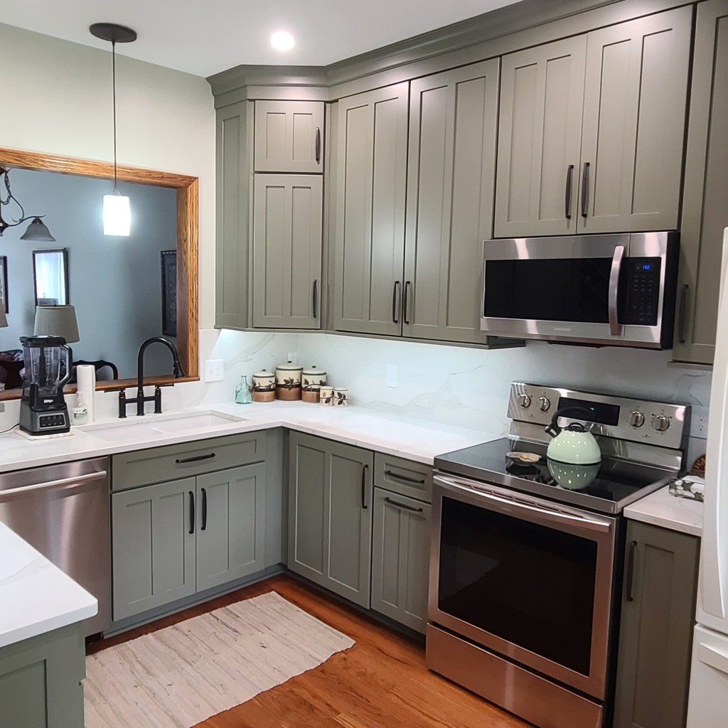Updated kitchen with sage green Shaker cabinets, white quartz countertops, stainless steel appliances, black faucet, and under-cabinet lighting.