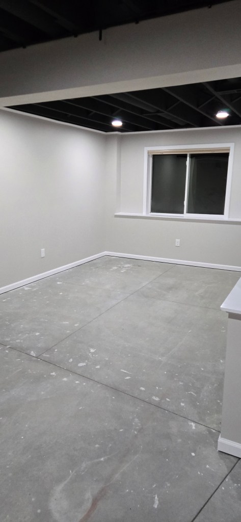 Finished basement room in Akron, Ohio with painted open ceiling, recessed lighting, smooth drywall, and concrete floor ready for flooring installation.