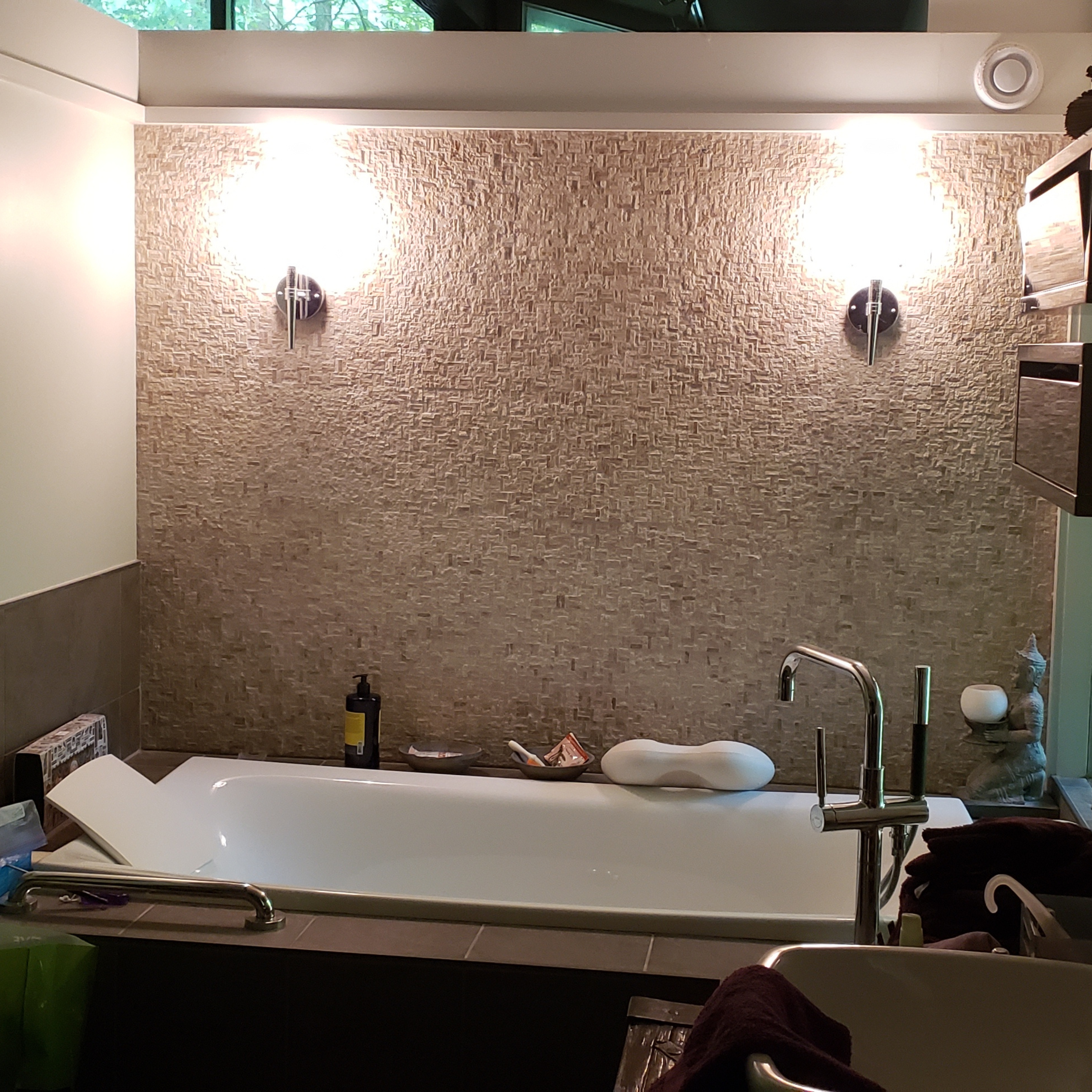 Textured tile wall behind a freestanding bathtub with modern wall-mounted sconces