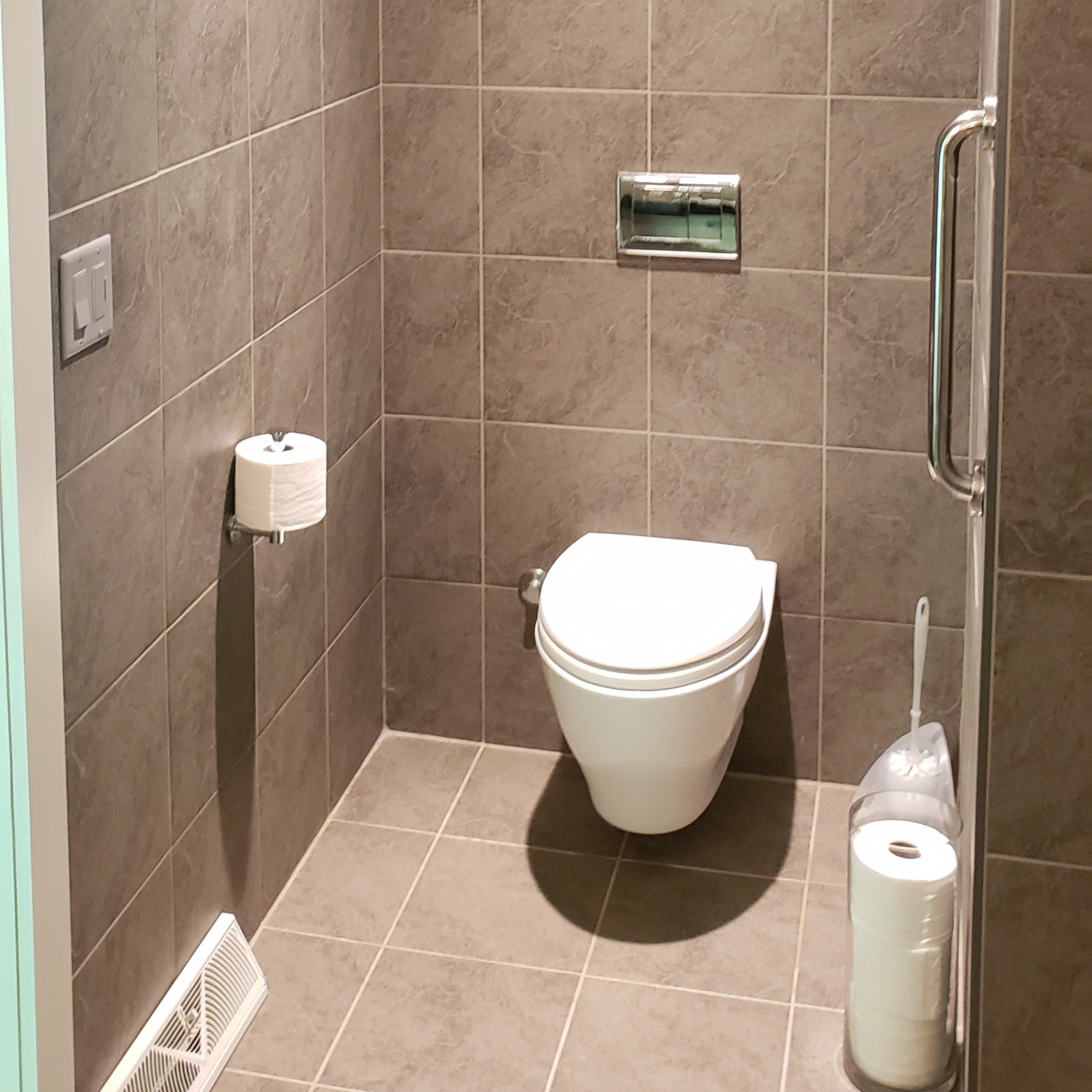 Wall-hung toilet with large-format tile walls in a modern bathroom remodel
