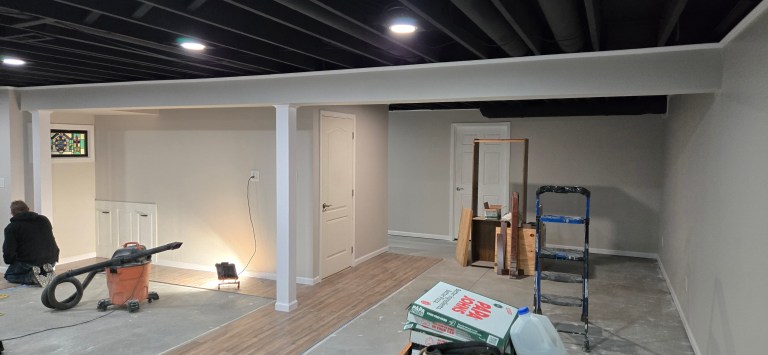 Basement remodel in progress in Akron, Ohio showing new framing, recessed lighting, painted ceilings, support columns, and updated flooring installed by a local remodeling contractor.