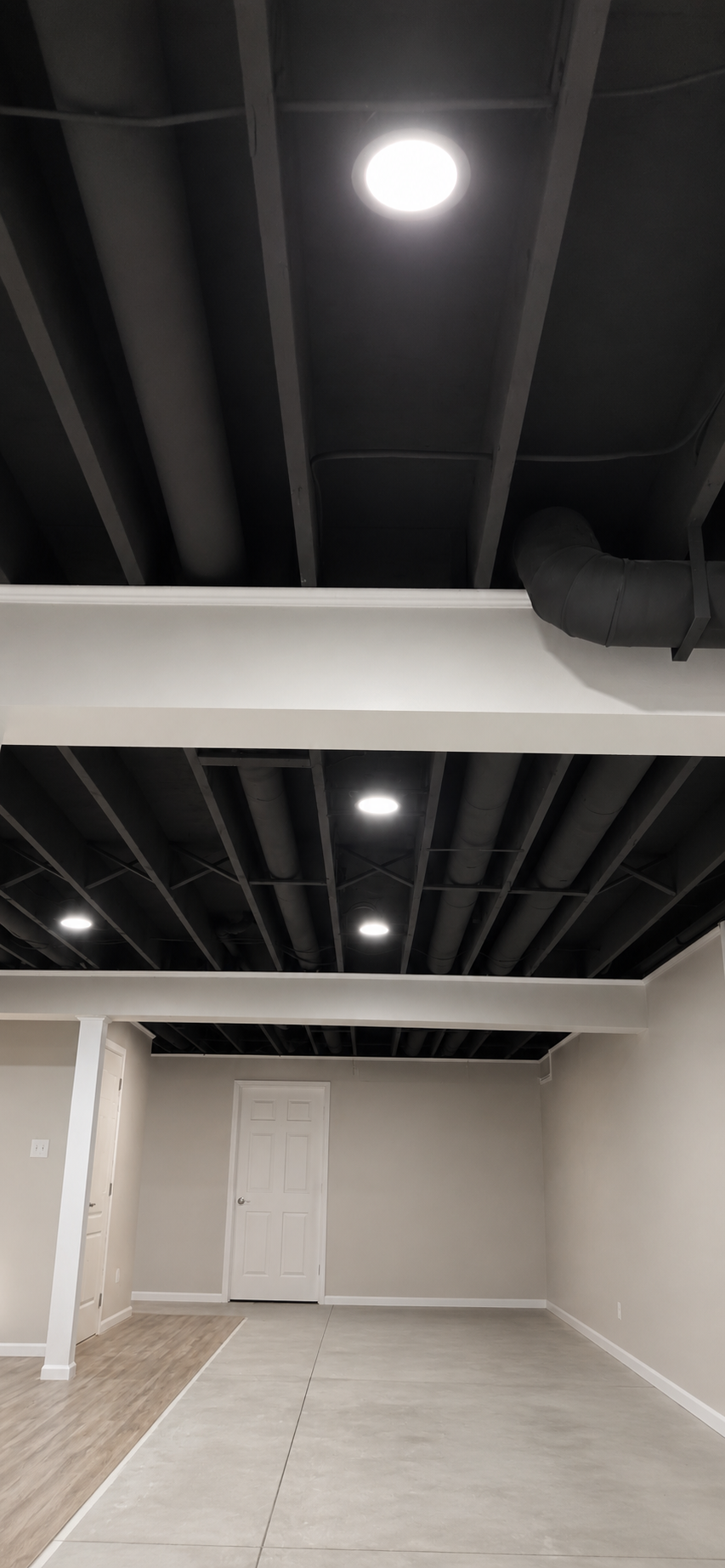 Basement remodel in Strongsville, Ohio by Butler Building featuring a black exposed ceiling, recessed lighting, finished walls, and updated basement flooring.