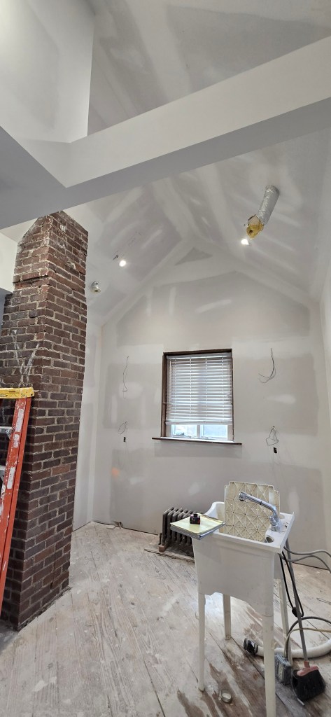 Kitchen remodel under construction featuring exposed brick chimney, vaulted ceiling framing, recessed lighting, drywall finishing, and utility sink in Akron, Ohio.