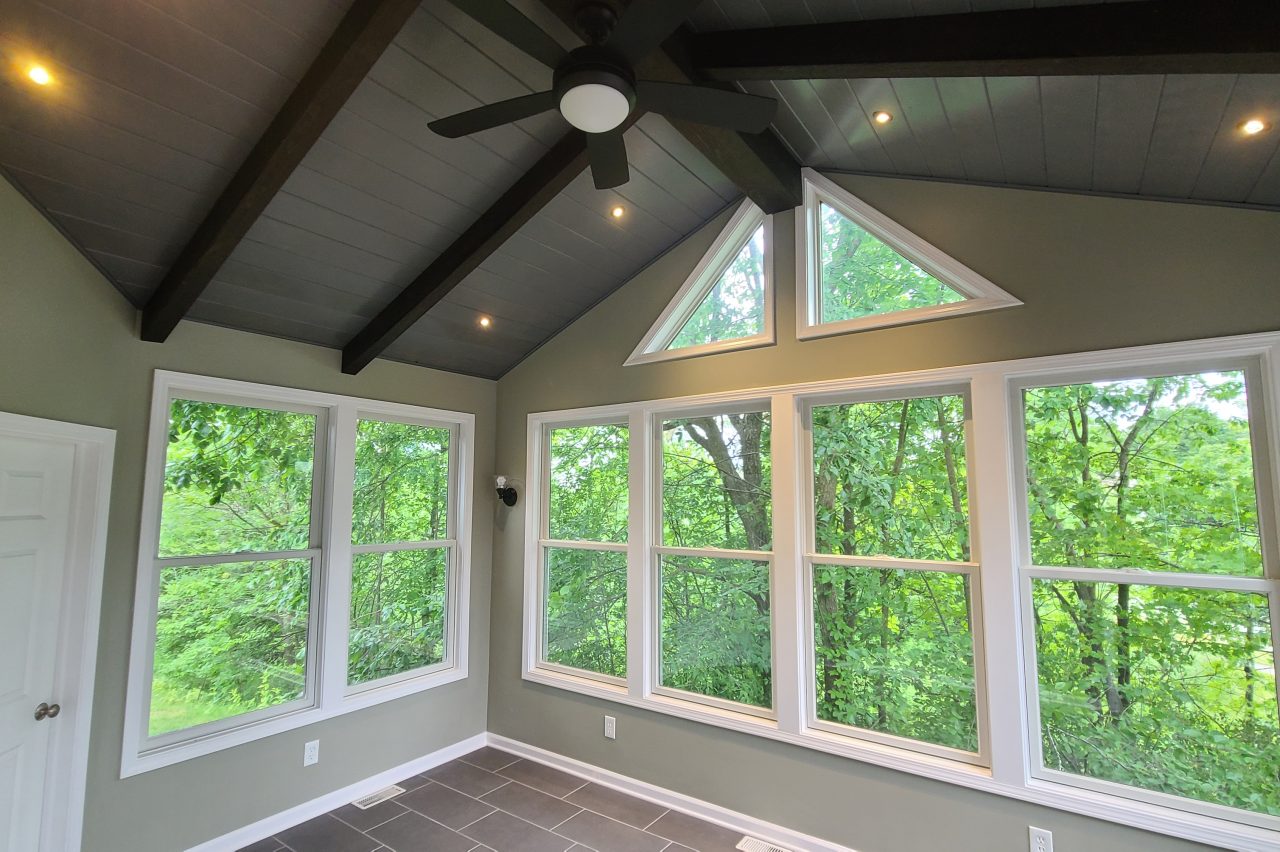 Four-season sunroom with vaulted ceiling, fan, and large windows overlooking trees